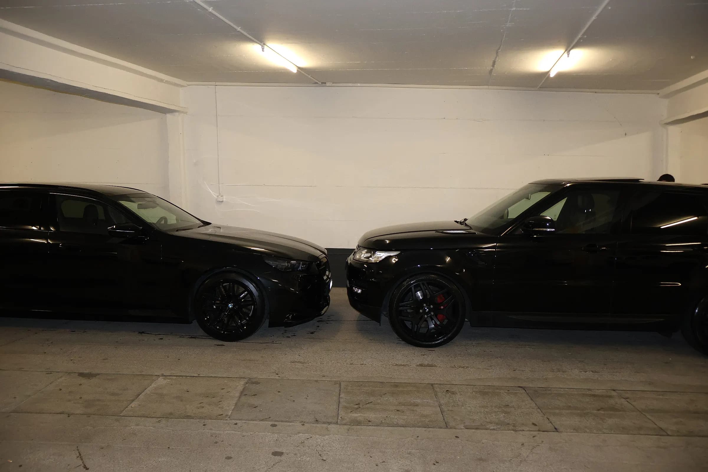 Zwei frisch aufbereitete schwarze Fahrzeuge Front an Front unter Werkstattlicht – BMW und Range Rover Sport nach dem Detailing durch HZZH